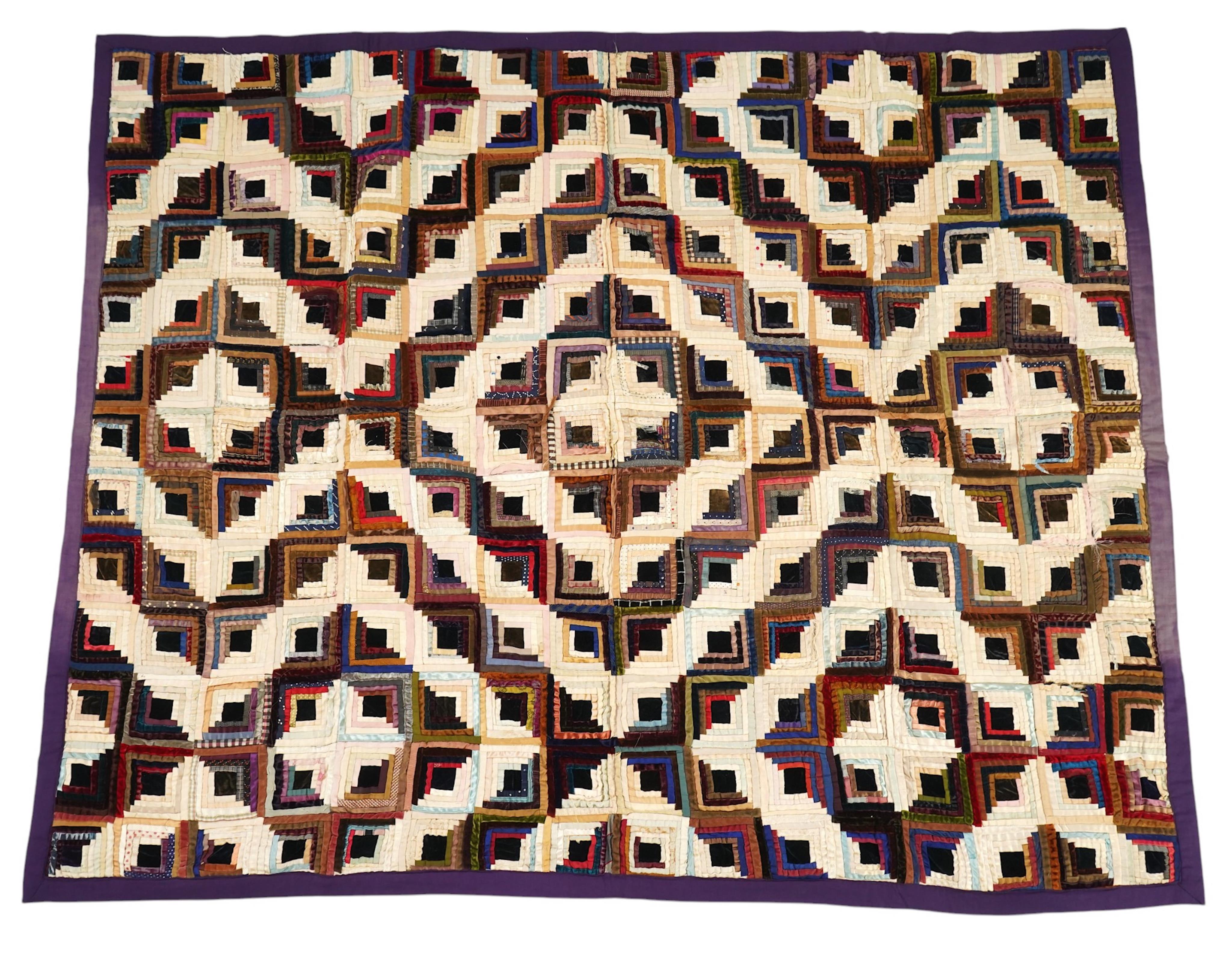 An early 20th century silk and velvet ‘Log Cabin’ designed bed cover, with a deep purple cotton backing, 140cm x 74cm. Condition - various thin strips have torn or are worn from constant use, so needs restoration.